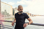Man looking at smartwatch on bridge, river and buildings in background, Berlin, Germany