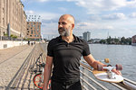 Man holding skateboard on bridge, river and buildings in background, Berlin, Germany