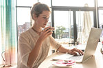 Young woman using laptop and having coffee in office on sunny day