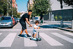Father helping son ride push scooter on pedestrian crossing