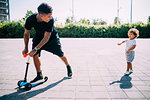 Father teaching son ride push scooter in park