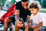 Father teaching son use smartphone on bench