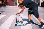 Father teaching son ride push scooter on pedestrian crossing