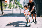 Father teaching son ride push scooter on sidewalk