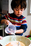 Toddler pouring water into flour in mixing bowl