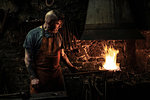 Mature male blacksmith heating metal on open fire in workshop