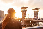 Female tourist with red hair looking out over Stanley bridge at sunset, rear view, Alexandria, Egypt