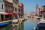Moored boats on canal, colourful residential buildings, houses, shops and clock tower, San Stefano Square, Murano Island, Venetian Lagoon, Veneto, Italy