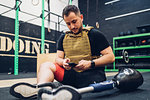 Man with prosthetic leg sitting on gym floor texting