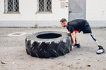 Man with prosthetic leg weight training with giant tyre