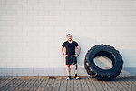 Man with prosthetic leg leaning on wall beside training tyre