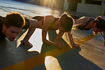 Friends doing plank in sports stadium at sunset