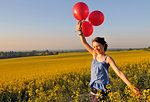 Girl with red balloons on rapeseed field, Eastbourne, East Sussex, United Kingdom