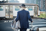 Senior businessman with wheeled luggage walking on pedestrian crossing, Milano, Lombardia, Italy