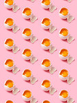 Broken eggs arranged in rows on pink background