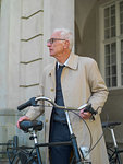 Senior man in raincoat holding bicycle, Copenhagen, Hovedstaden, Denmark