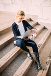 Young woman sitting on city stairway looking at laptop