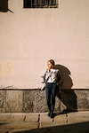 Young woman leaning against sunlit city wall