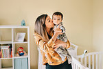 Mother kissing baby son in nursery, portrait