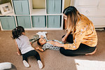 Girl crawling on nursery floor while mother dressing baby brother