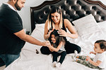 Baby boy sitting on bed while mother and father play with sister