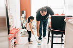 Girl sweeping kitchen floor, father watching