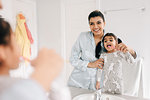 Girl with mother brushing her teeth in bathroom mirror, over shoulder view