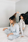Girl brushing mother's hair on bed in morning