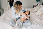 Girl being tickled by her mother on bed in morning