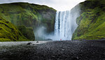 Visitor dwarfed by plunging waters of Skogafoss, Iceland's most iconic waterfall, situated on the Skoga River, Southern Region, Iceland, Polar Regions