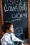 Boy in school uniform beside blackboard at home