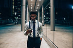 Businessman using smartphone, walking past mirrored wall of office building, Milano, Lombardia, Italy