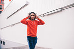 Young man putting on headphones walking past concrete wall