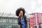 Happy young woman with afro hair in city, laughing and making smartphone call