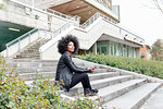 Young woman with afro hair sitting on city stairway looking away