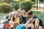 Group of friends relaxing, blowing bubbles at picnic in park