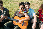 Friends relaxing, playing guitar in park