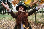 Young woman with long red hair throwing autumn leaves in park