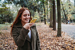 Young woman with long red hair taking smartphone selfie in autumn park