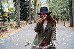 Young woman with long red hair on bicycle looking at smartphone in autumn park, Florence, Tuscany, Italy