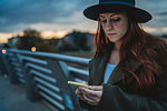Young woman with long red hair on footbridge looking at smartphone at dusk, Florence, Tuscany, Italy
