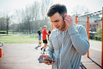 Calisthenics class at outdoor gym, young man putting in earphones