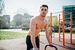 Calisthenics at outdoor gym, bare chested young man preparing to use exercise equipment