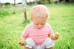 Cute female toddler squatting on grass looking down