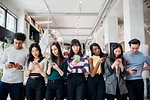 Group of young businesswomen and men in a row, looking at smartphones