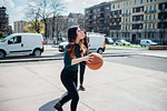 Young female friends playing basketball on city court