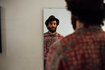 Bearded young man looking into mirror at home