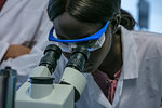 Young female scientist looking through microscope in laboratory, close up