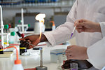 Young male and female scientists using pipette and bunsen burner in laboratory experiment, cropped