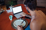Mid adult man typing on laptop at breakfast table